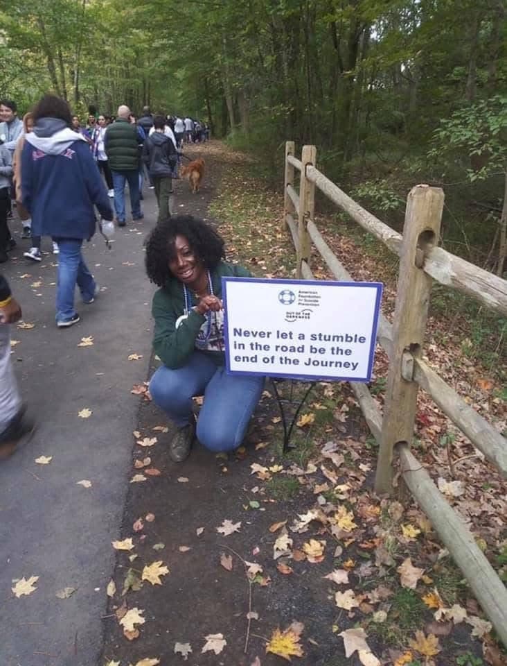 Dr. Tracy beside a sign that reads Never let a stumble in the road be the end of the journey